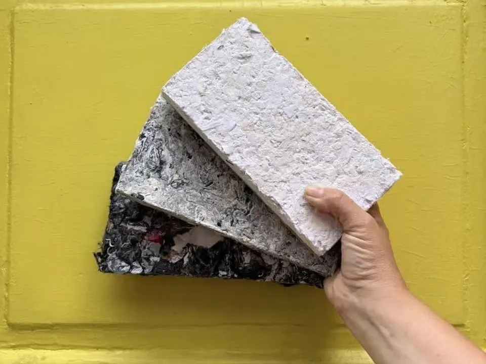 Una mano sostiene tres muestras de paneles Requecho de distintos acabados frente a una puerta amarilla.