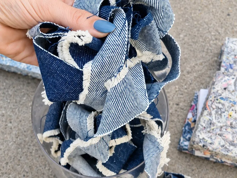 Una mano sostiene retazos de tela de jean, el descarte textil que se vuelve panel, con paneles Requecho de fondo.