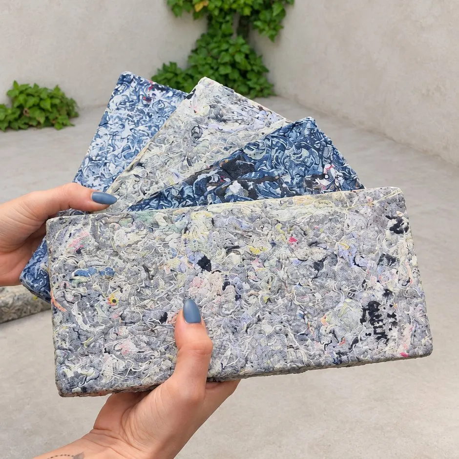 Manos que despliegan en abanico paneles Requecho en distintos tonos de azul, en un patio con hiedra.